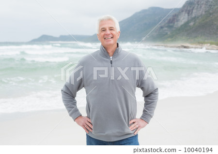 Happy senior man with hands on hips at beach Happy senior man with hands on hips at beach 10040194
