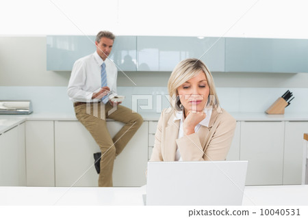 Woman using laptop and man in background at kitchen Woman using laptop and man in background at kitchen 10040531