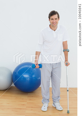 Portrait of a smiling man with crutch and dumbbell Portrait of a smiling man with crutch and dumbbell 10040841