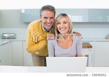 Happy casual couple with laptop in kitchen Happy casual couple with laptop in kitchen 10040842