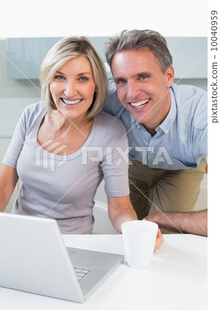 Happy casual couple using laptop in kitchen 10040959