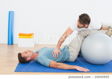 Physical therapist assisting young man with yoga ball 10040995
