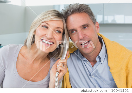 Close-up of a happy couple using telephone in kitchen 10041301