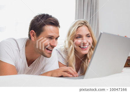 Cheerful relaxed couple using laptop in bed Cheerful relaxed couple using laptop in bed 10047166