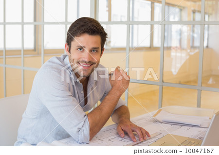 Smiling businessman working on blueprints in office Smiling businessman working on blueprints in office 10047167