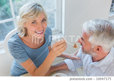Smiling woman feeding mature man pastry 10047175