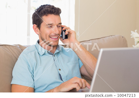 Happy man using laptop and mobile phone on couch Happy man using laptop and mobile phone on couch 10047213