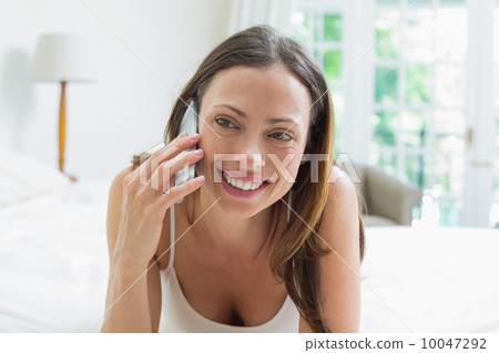 Smiling woman using mobile phone in bed Smiling woman using mobile phone in bed 10047292