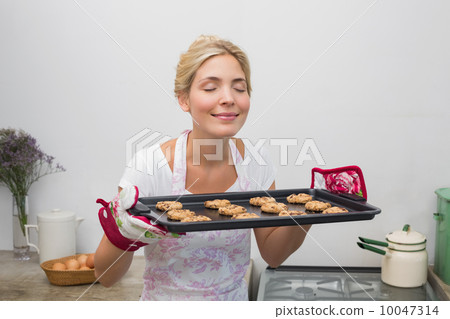 Woman holding a tray of cookies with eyes closed in kitchen 10047314