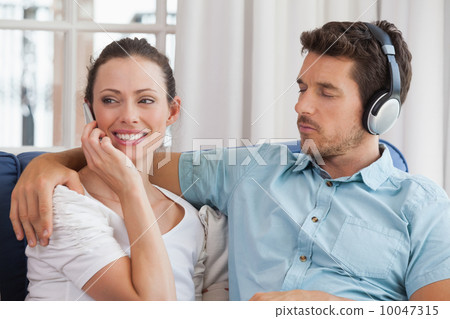 Couple with mobile phone and headphones in living room 10047315