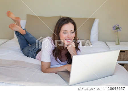 Smiling relaxed woman using laptop in bed Smiling relaxed woman using laptop in bed 10047657