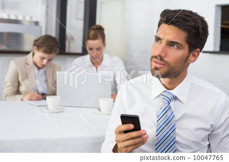 Businessman text messaging with colleagues at office desk Businessman text messaging with colleagues at office desk 10047765