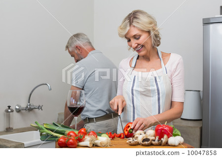 Happy mature couple preparing food together in kitchen Happy mature couple preparing food together in kitchen 10047858