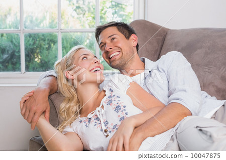 Cheerful casual couple laughing in living room Cheerful casual couple laughing in living room 10047875