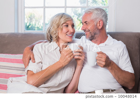 Relaxed mature couple with coffee cups in living room 10048014