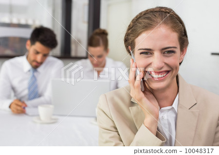 Businesswoman using mobile phone with colleagues at office desk Businesswoman using mobile phone with colleagues at office desk 10048317