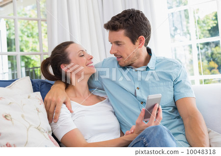 Happy couple text messaging in living room Happy couple text messaging in living room 10048318