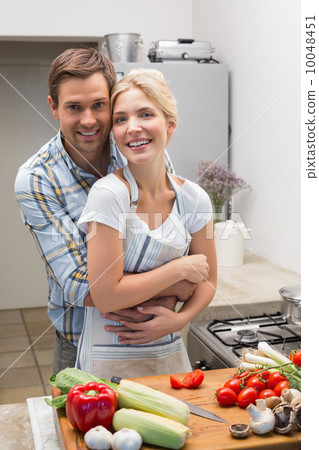 Portrait of a couple embracing while preparing food in kitchen Portrait of a couple embracing while preparing food in kitchen 10048451