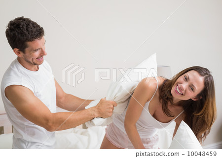 Cheerful couple pillow fighting in bed Cheerful couple pillow fighting in bed 10048459