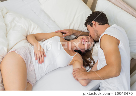 Man kissing womans forehead as she sleeps in bed Man kissing womans forehead as she sleeps in bed 10048470