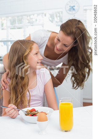 Mother looking at daughter while having breakfast in kitchen Mother looking at daughter while having breakfast in kitchen 10048602