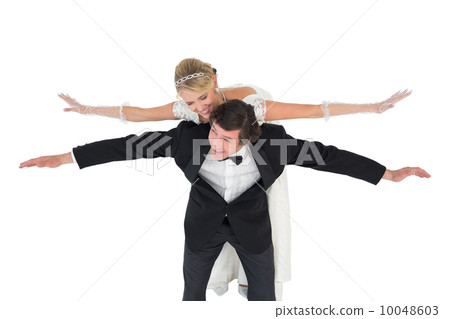 Happy groom with arms outstretched carrying bride on back Happy groom with arms outstretched carrying bride on back 10048603