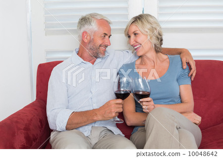 Relaxed mature couple toasting wine glasses in living room Relaxed mature couple toasting wine glasses in living room 10048642