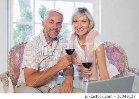 Relaxed mature couple with wine glass using laptop Relaxed mature couple with wine glass using laptop 10049127