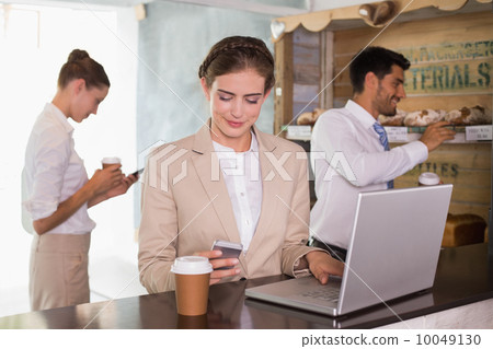 Businesswoman using mobile phone and laptop in office cafeteria Businesswoman using mobile phone and laptop in office cafeteria 10049130