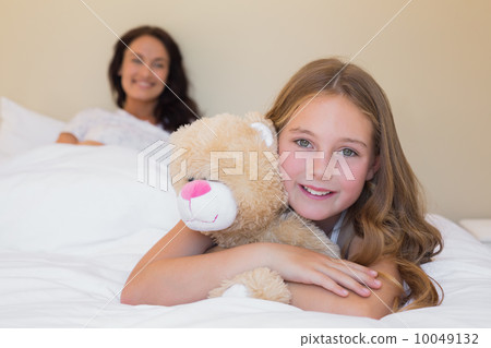 Little girl embracing teddy bear with mother in background Little girl embracing teddy bear with mother in background 10049132
