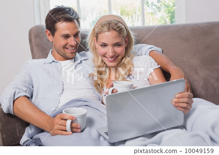 Relaxed couple with coffee cups using laptop on sofa Relaxed couple with coffee cups using laptop on sofa 10049159