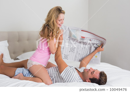 Woman sitting on man as he reads newspaper in bed Woman sitting on man as he reads newspaper in bed 10049476