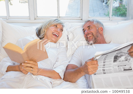 Cheerful mature couple with newspaper and book in bed Cheerful mature couple with newspaper and book in bed 10049538