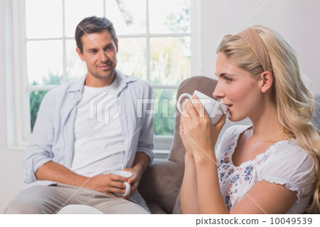 Relaxed couple with coffee cups sitting in living room Relaxed couple with coffee cups sitting in living room 10049539
