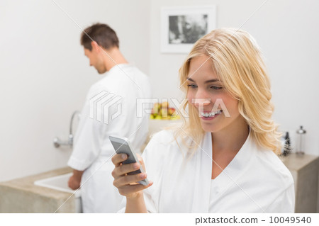 Smiling woman text messaging with man in background at kitchen Smiling woman text messaging with man in background at kitchen 10049540