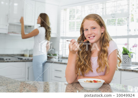 Girl having breakfast with mother in background at kitchen 10049924
