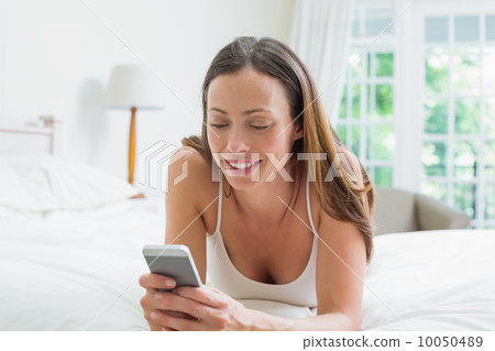 Smiling young woman text messaging in bed 10050489