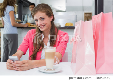 Smiling woman using mobile phone in coffee shop Smiling woman using mobile phone in coffee shop 10050659