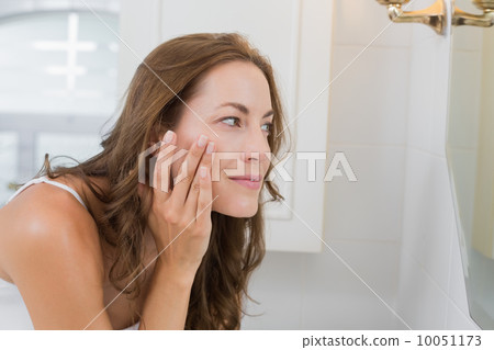 Side view of a beautiful young woman examining her face Side view of a beautiful young woman examining her face 10051173