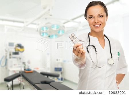 Young positive brunette doctor woman holding pills in surgery room interior 10088901