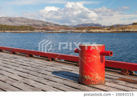 Red mooring bollard on wooden pier with seascape on a background 10093555