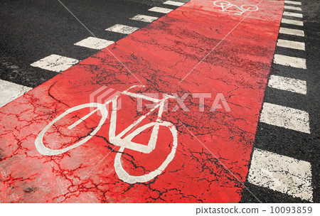 Red bicycle road marking on urban asphalt road crossing 10093859