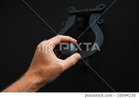 Male hand knocking old black metal door 10094230