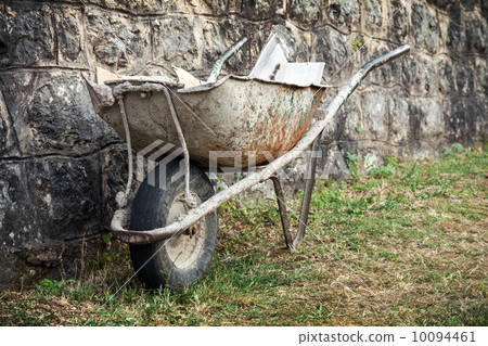 Old construction wheelbarrow stands against the wall 10094461