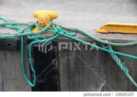 Yellow mooring bollard with green naval rope on the pier 10095107