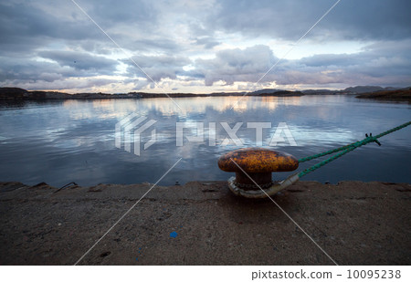 Old rusted yellow mooring bollard with rope at night 10095238