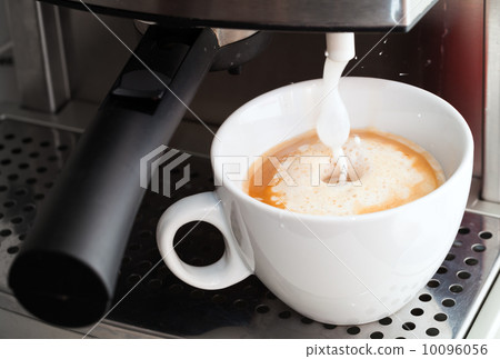 Coffee maker pouring hot milk foam in espresso coffee to prepare cappuccino 10096056