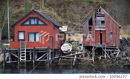 Traditional Norwegian red wooden boat barns on the sea coast. Old and new one next to 10096237