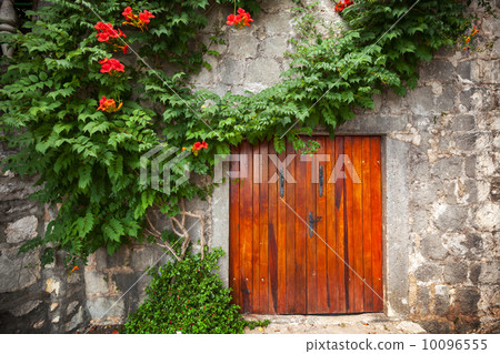 Red wooden gate in old stone wall with decorative flowers. Peras 10096555