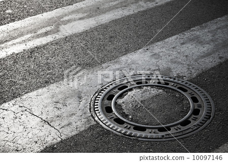 Sewer manhole cover on dark asphalt road with pedestrian crossin Sewer manhole cover on dark asphalt road with pedestrian crossin 10097146